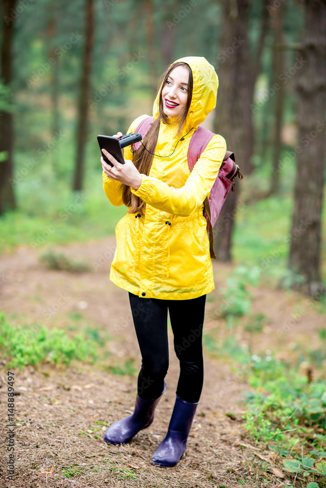 穿着黄色雨衣的年轻女子在绿松f中行走时使用智能手机进行定向