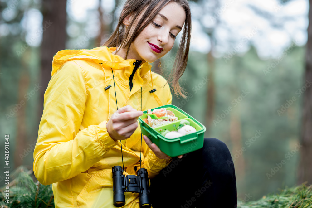 一名年轻女子在森林中旅行时吃了一份午餐盒里有健康食品的零食