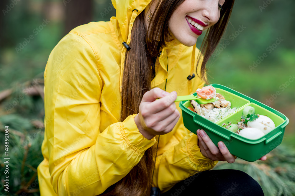 一名年轻女子在森林中旅行时，在午餐盒里放着健康食品吃零食