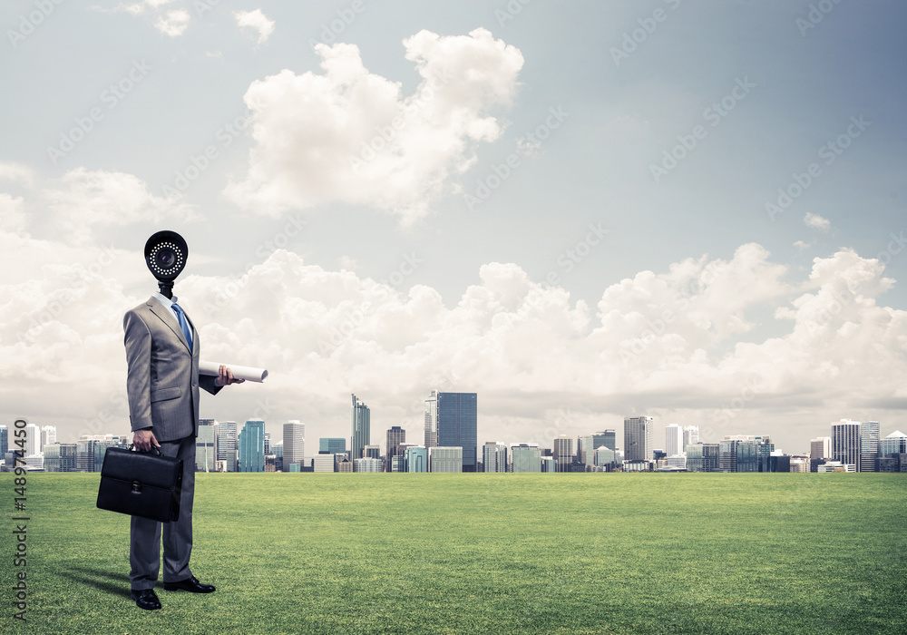 Camera headed man standing on green grass against modern citysca