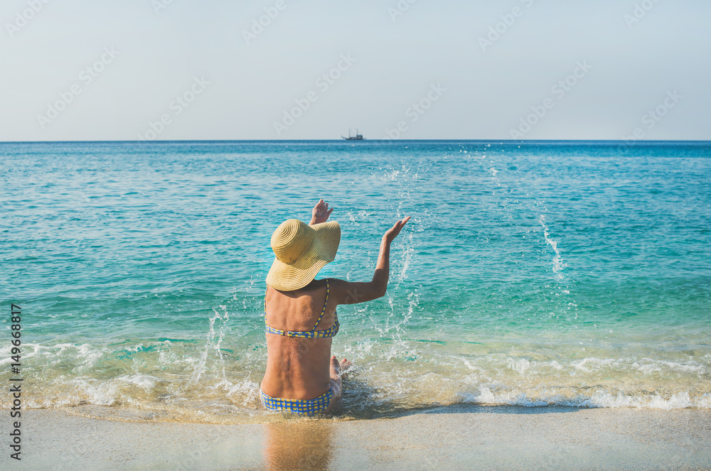 美丽苗条的高级女游客穿着比基尼坐在沙滩上，在Meditteranean度假胜地享受大海