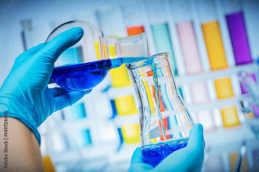 Scientist holding testing tube and flask with liquids.