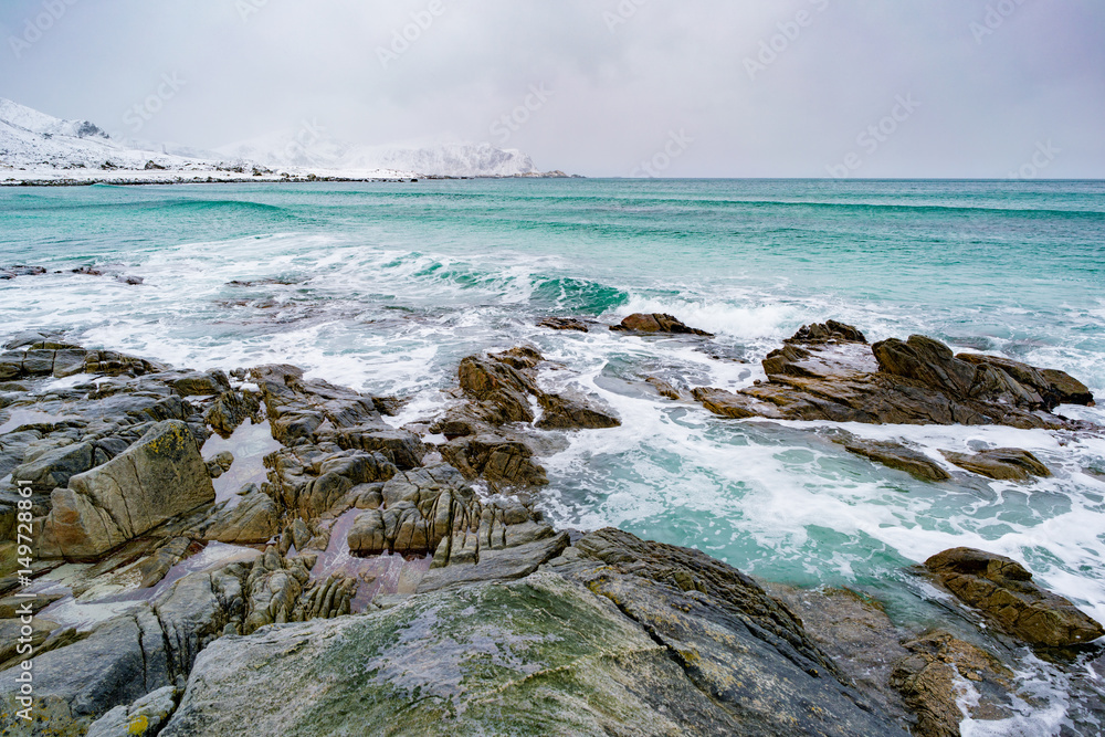 日出在大海和山脉的石头海岸，地平线上有雪