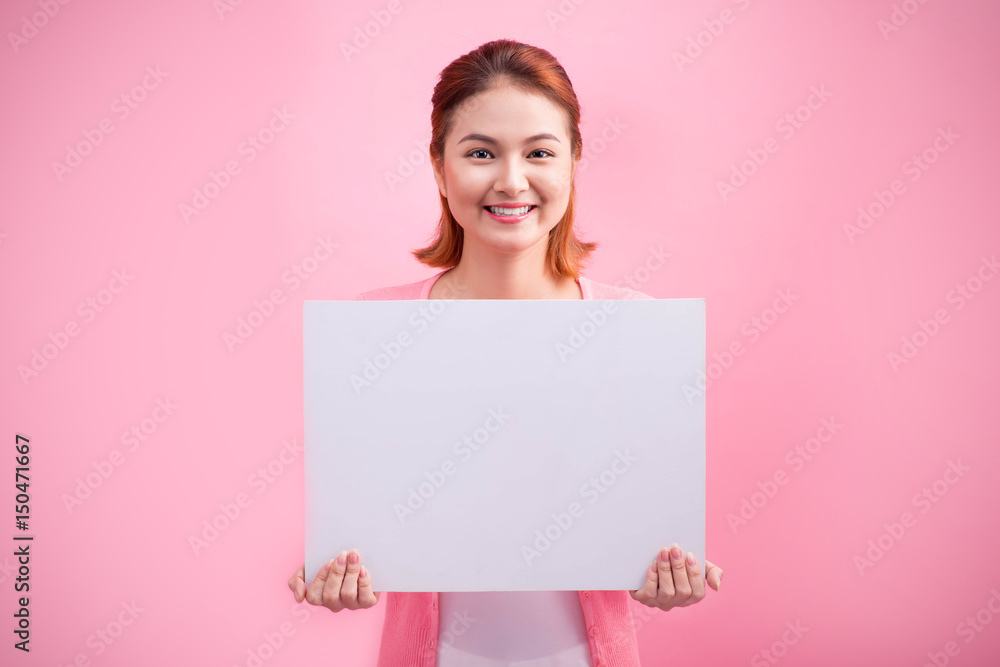 Cheerful beautiful asian young woman holding blank board on pink background.