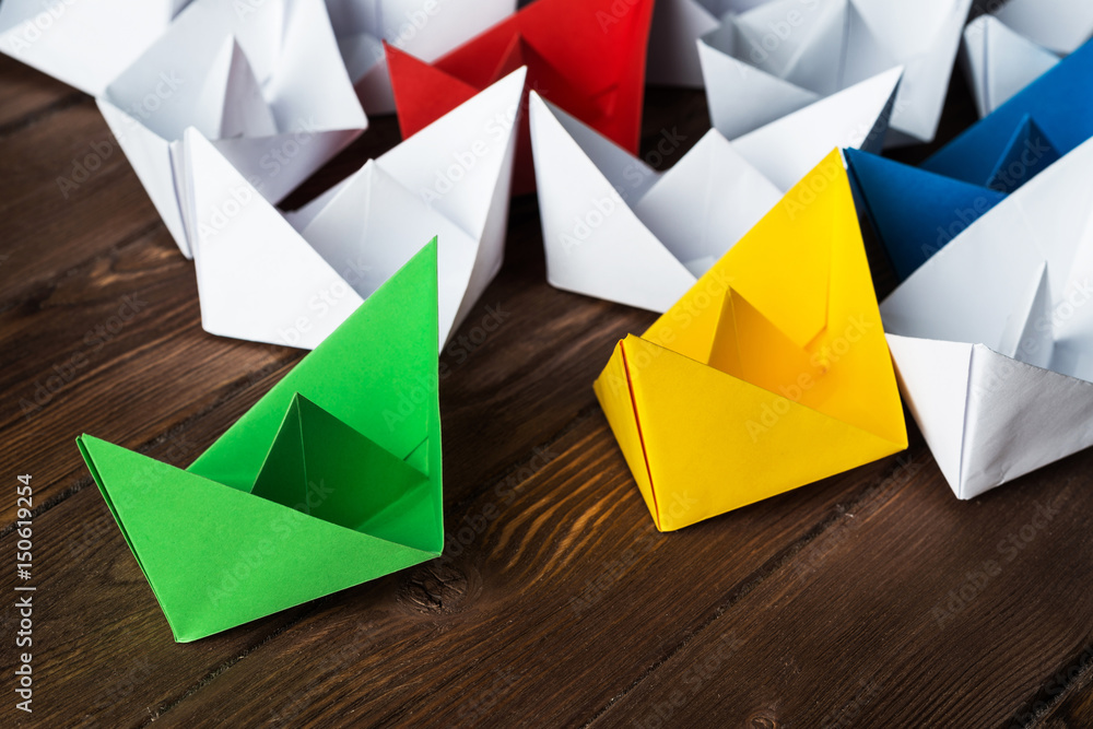 Business leadership concept with white and color paper boats on wooden table