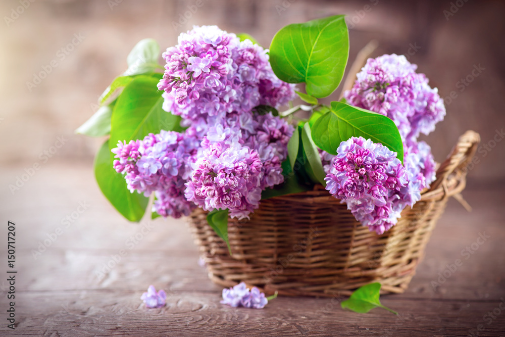 Lilac flowers bunch in a basket over blurred wood background