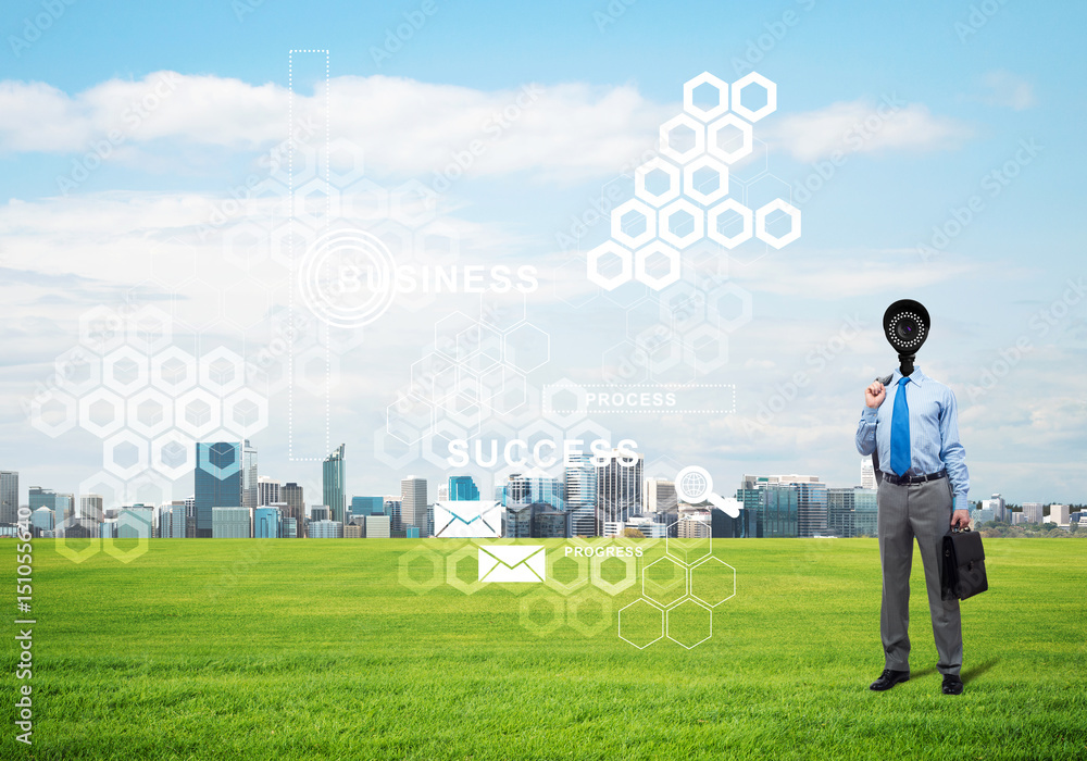 Camera headed man standing on green grass against modern cityscape