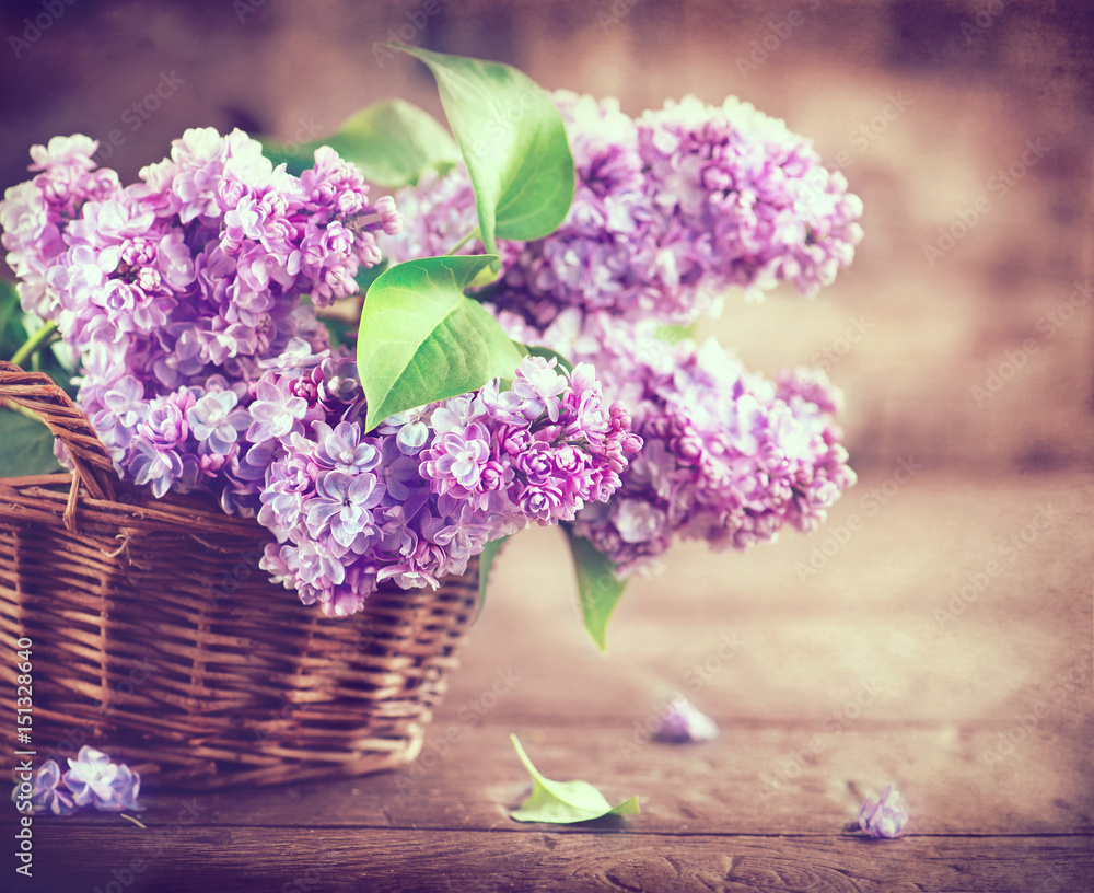 Lilac flowers bunch in a basket over blurred wood background