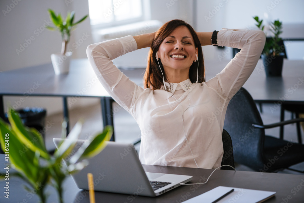 Young cheerful businesswoman listening music via headphones at office