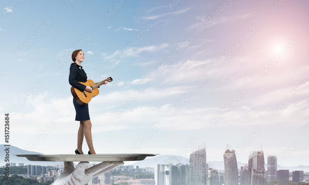 Attractive businesswoman on metal tray playing acoustic guitar against cityscape background