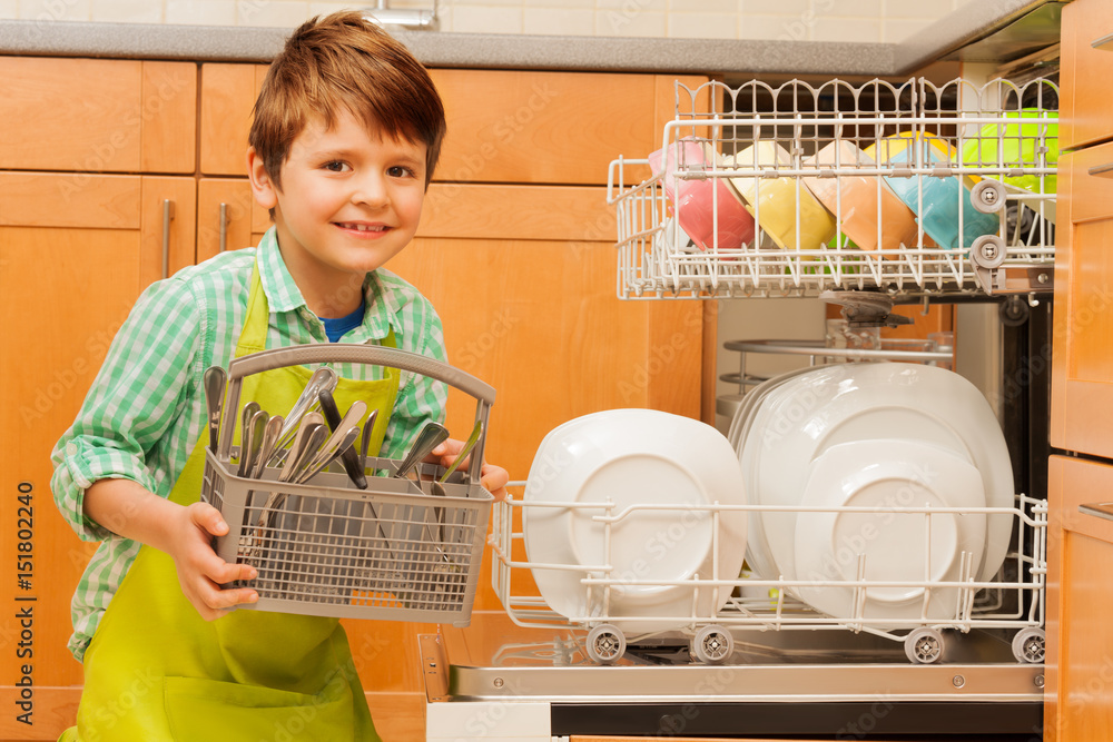 Happy boy pulling out cutlery of the dishwasher