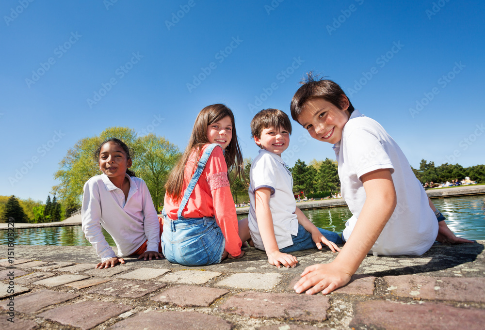 Four kids sitting on embankment during summer time