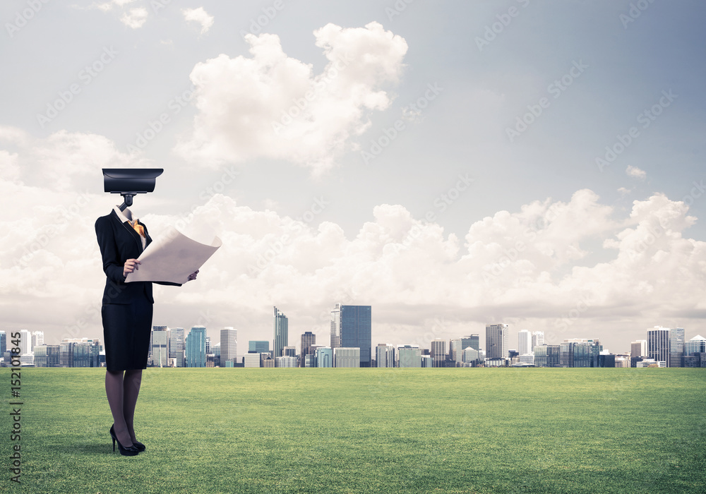 Camera headed woman standing on green grass against modern citys