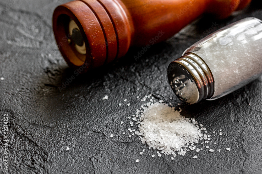 salt in glass bottle with saltcellar on black stone table background