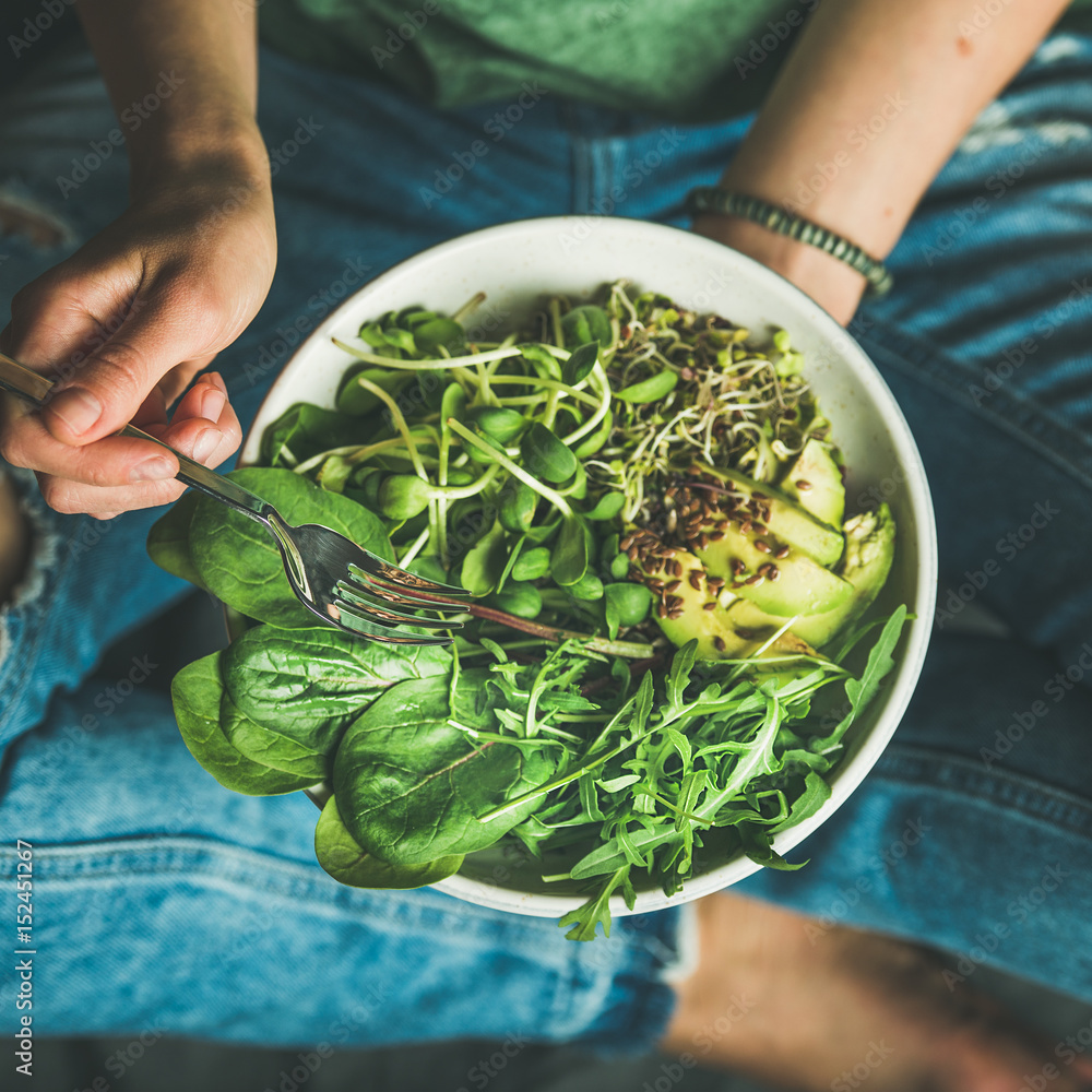 Green vegan breakfast meal in bowl with spinach, arugula, avocado, seeds and sprouts. Girl in jeans 