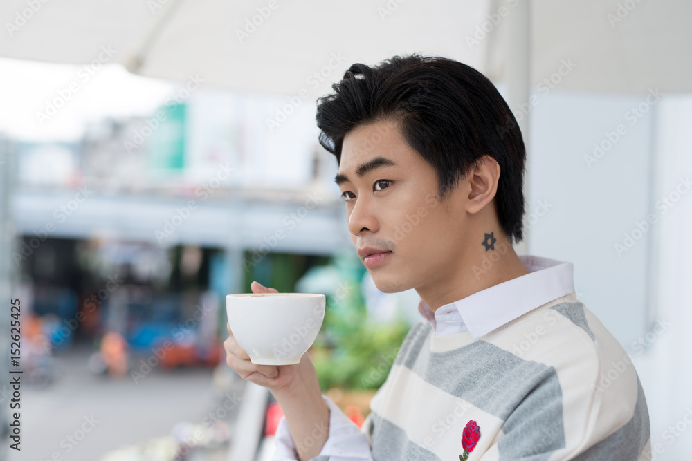 Handsome young man drinking coffee looking out at the view from his home office