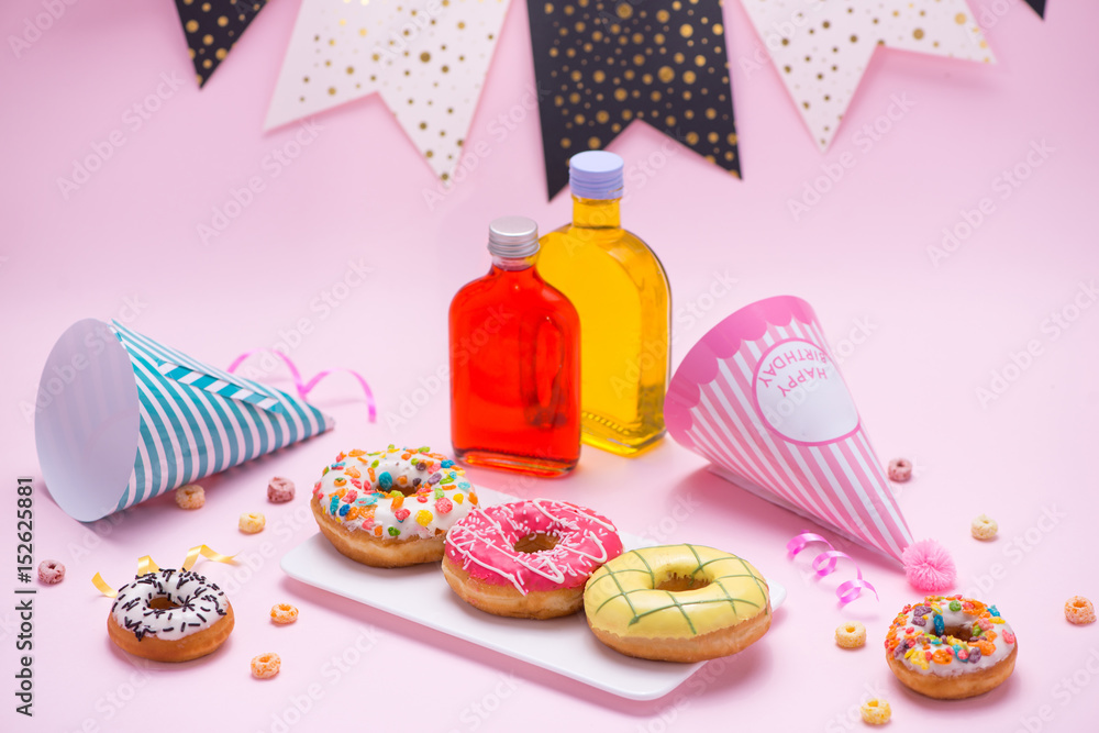 Party. Different colourful sugary round glazed donuts and bottles of drinks on pink background.