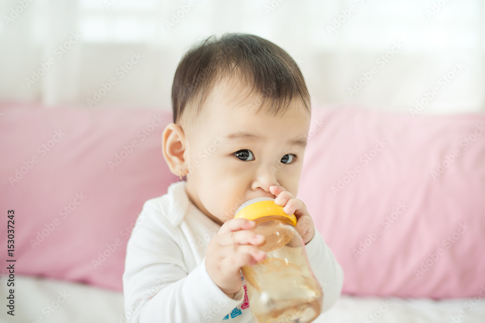 Sweet baby girl sucking milk in bottle at home.