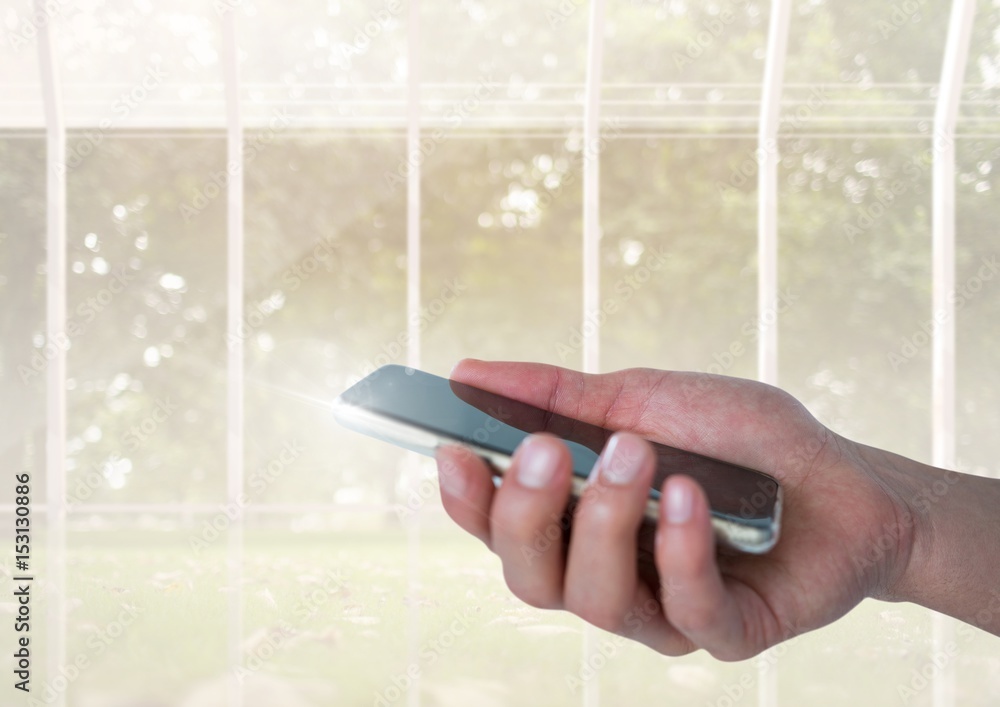 Hand with mobile phone and windows with trees