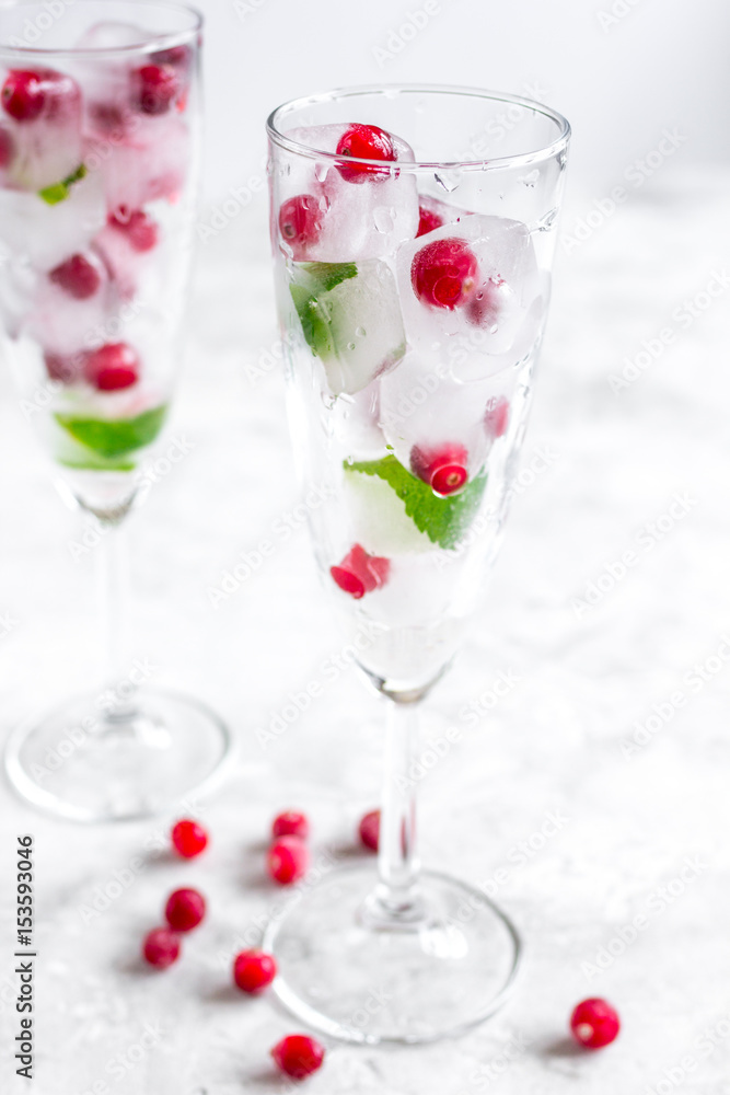 frozen red berries in ice cubes with mint in glasses on stone background