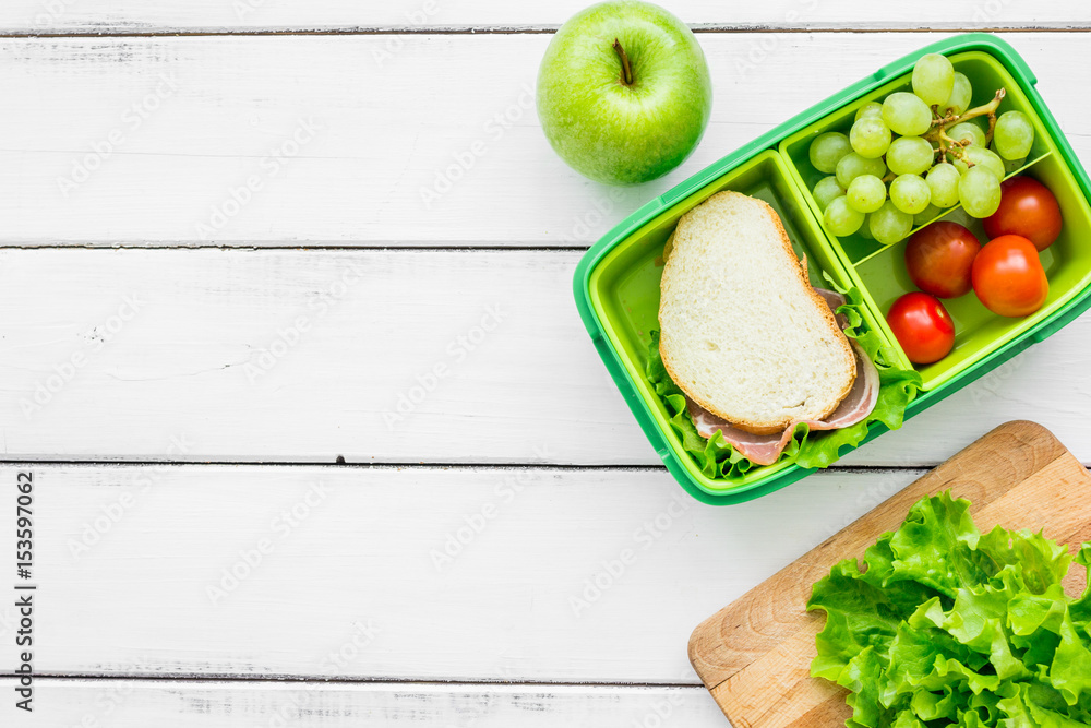 homemade lunch with apple, grape and sandwich in green lunchbox top view mockup