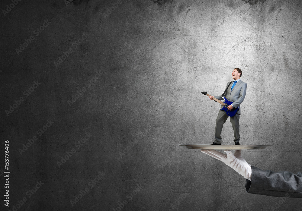 Businessman on metal tray playing electric guitar against concrete background