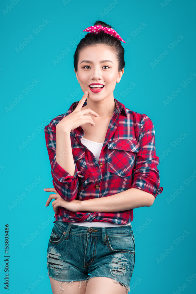 Smiling lovely asian woman dressed in pin-up style dress over blue.