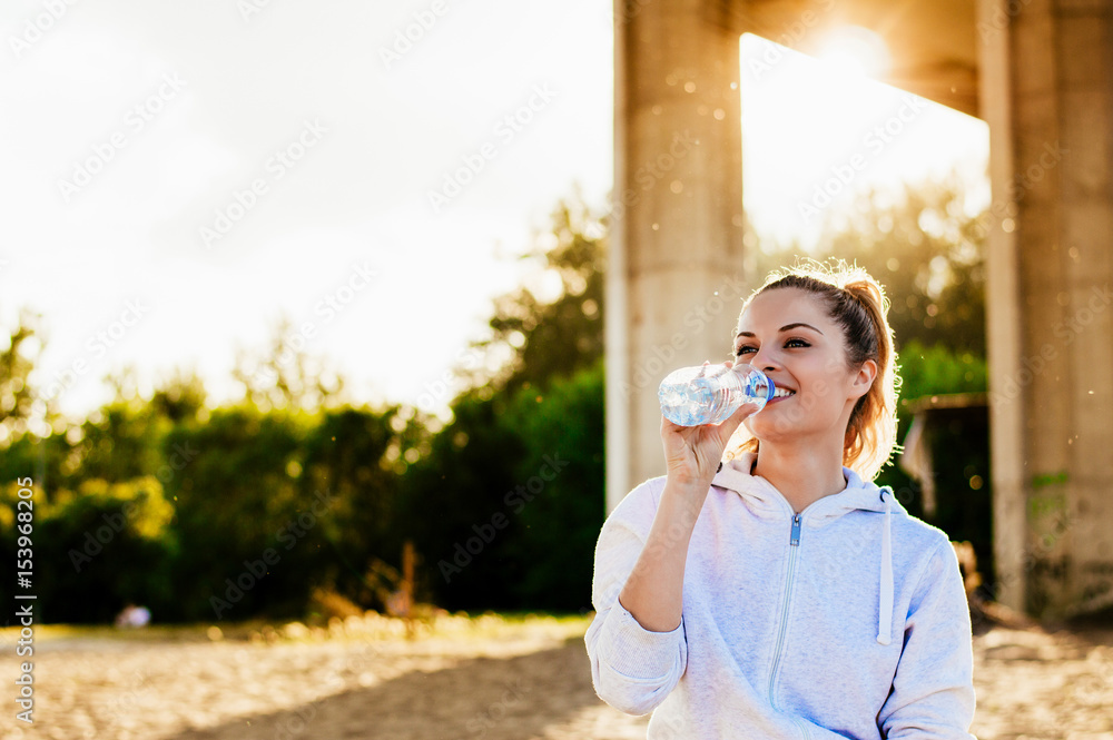 Beautiful girl in sport clothes drinking water after workout on the beach