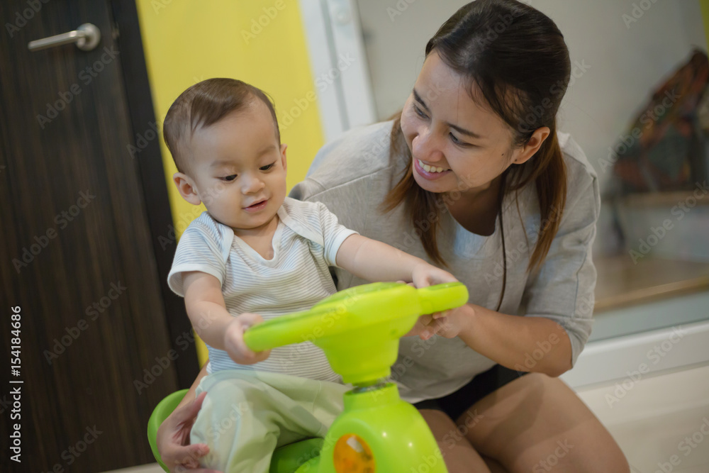 Happy Asian baby boy playing bike toy with his mother