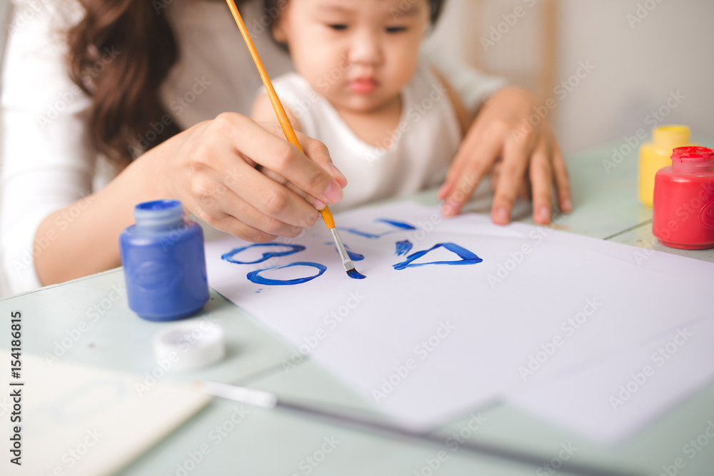 幸福的家庭，母亲和女儿一起画画。亚洲妇女帮助她的小女儿。