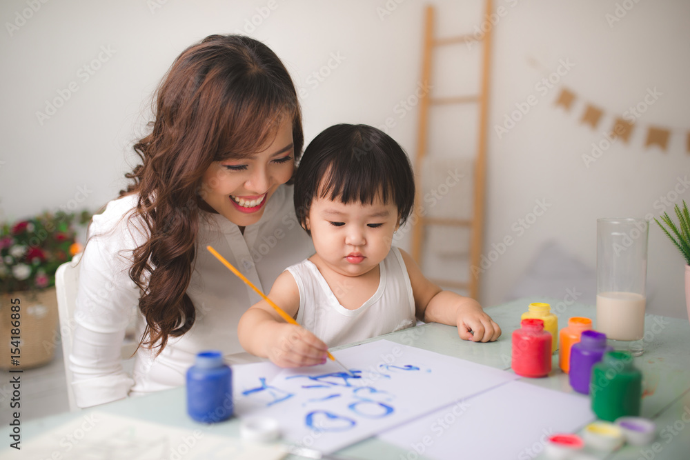 Happy family mother and daughter together paint. Asian woman helps her child girl.