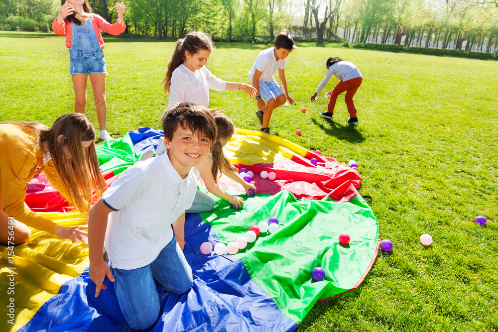 Cute boy sitting in center of rainbow parachute