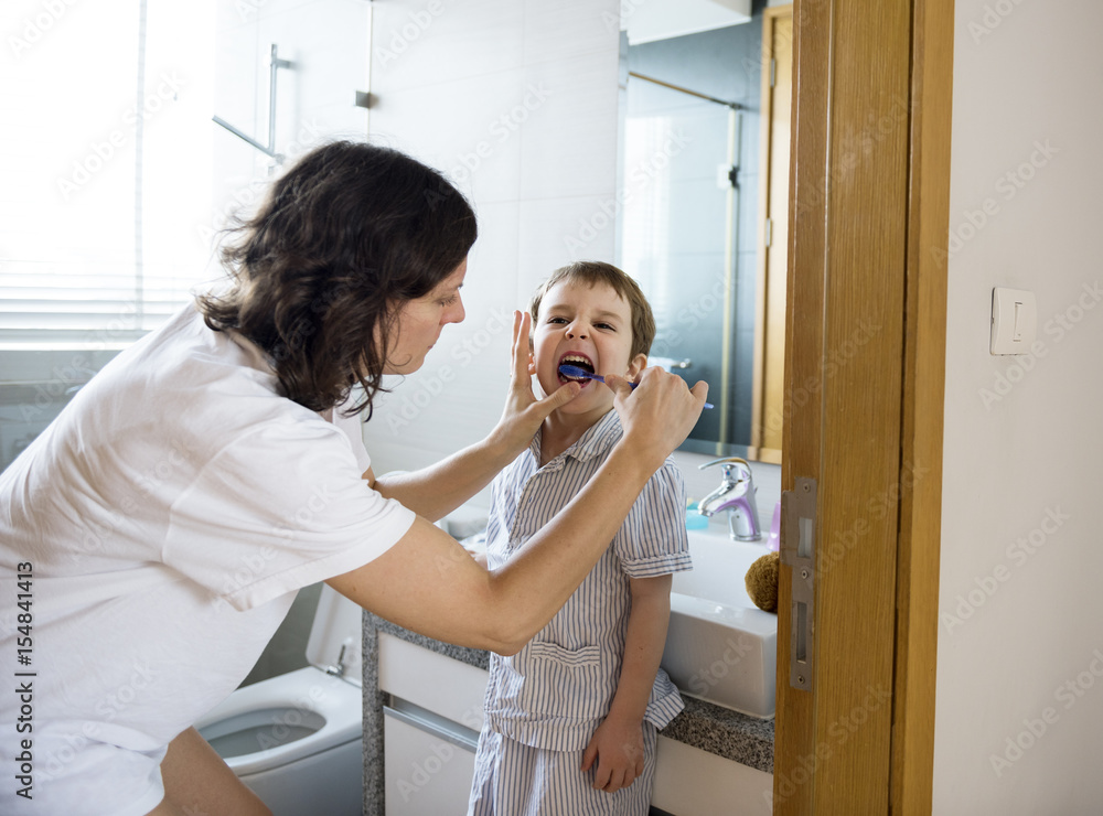 Mother teaching and helping the son how to brush his teeth