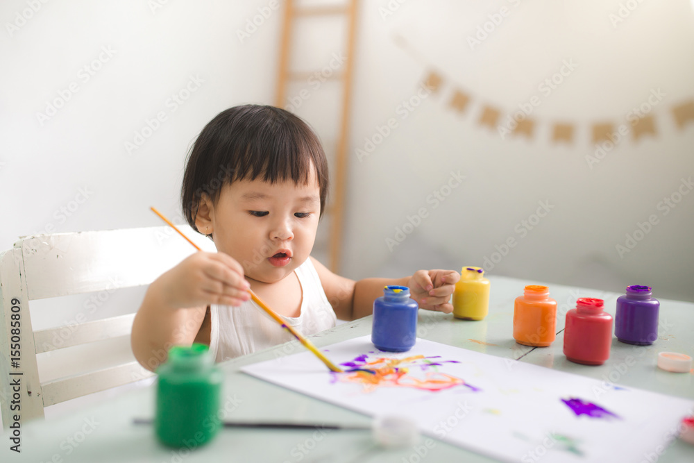 Funny laughing asian baby girl drawing with colorful pencils at home