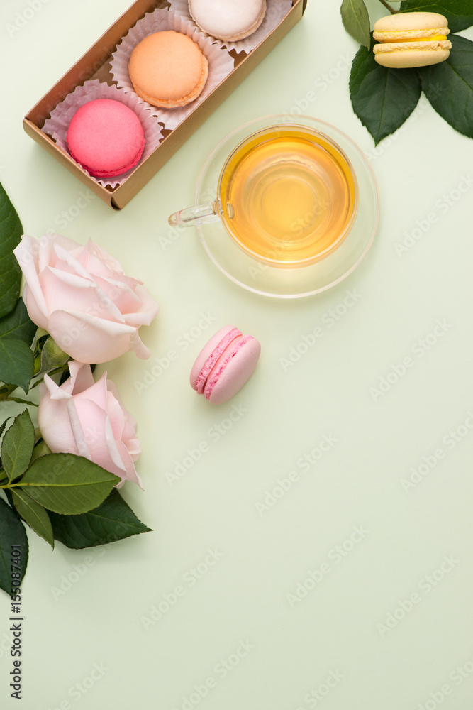 French macaroons. Many variegated sweet macarons in box with bouquet of pink roses on the table