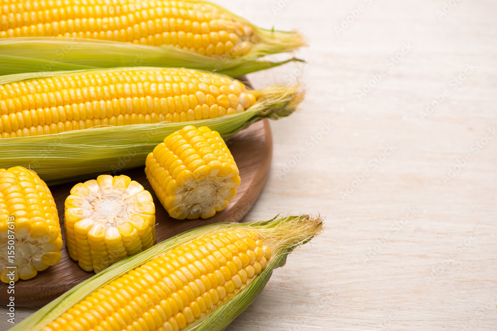 Sweet corn on cobs on cutting board on wooden table.