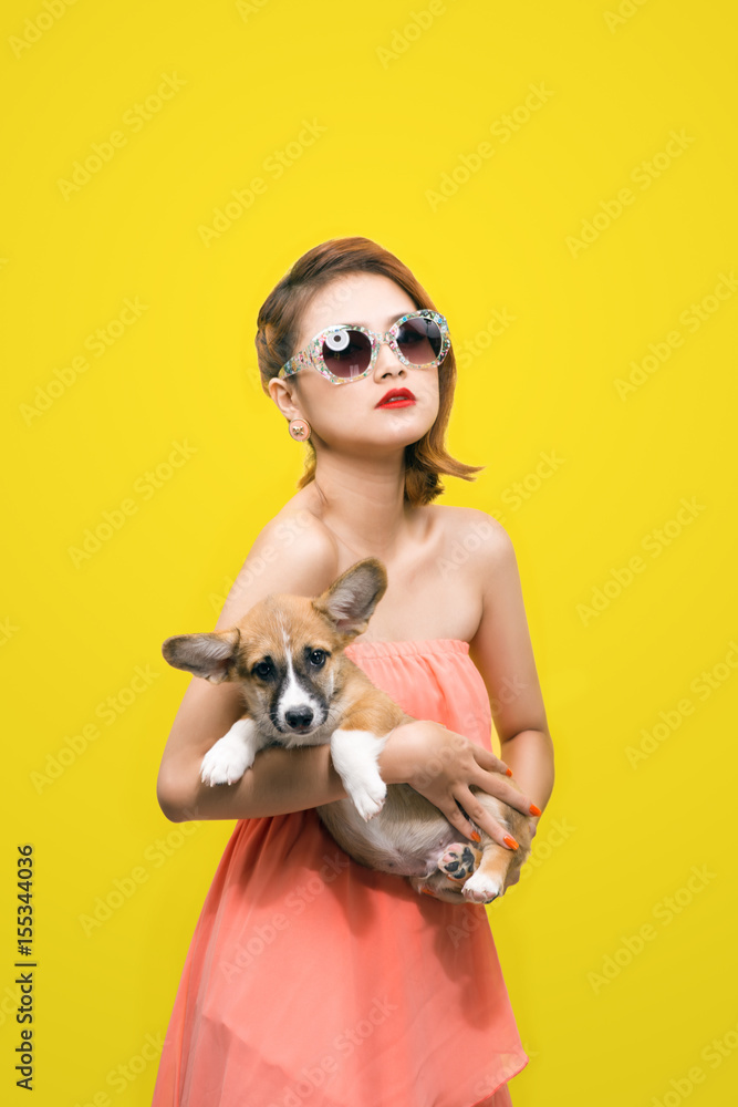 Beautiful young asian woman in nice spring dress, posing in studio with corgi puppy. Fashion photo.