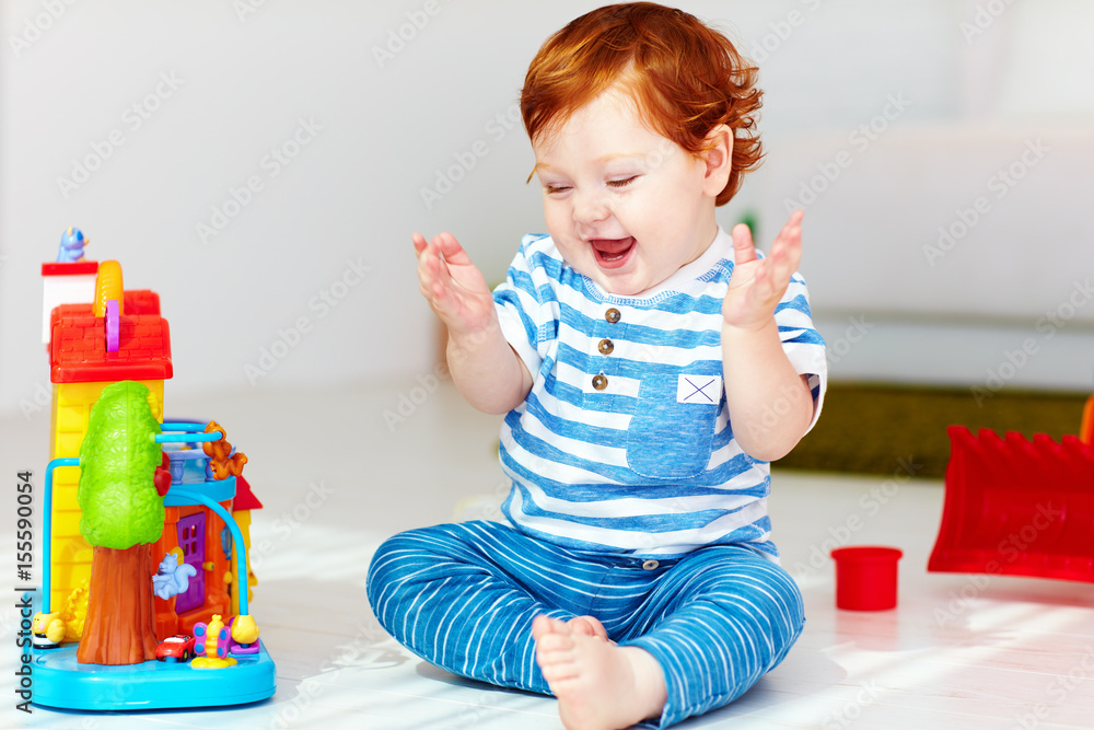 happy little redhead baby playing with toy house