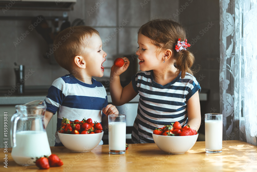 Happy children brother and sister eating strawberries with milk