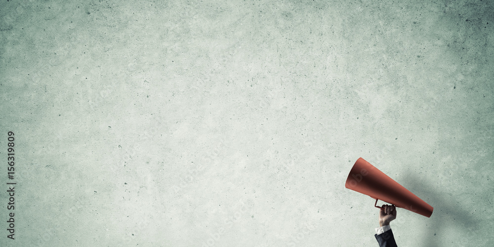 Hand of businesswoman holding red paper trumpet against concrete background