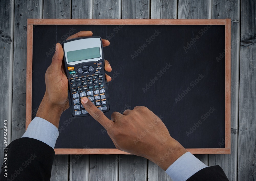 Hands with calculator against chalkboard and grey wood panel