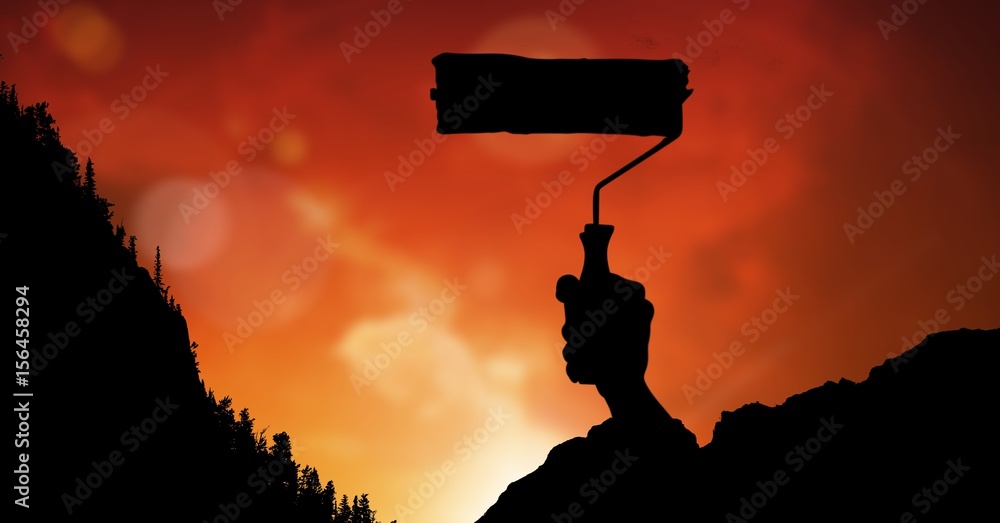 Silhouette image of hand holding paint roller against red sky