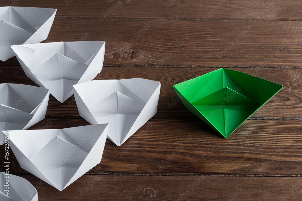 Business leadership concept with white and color paper boats on wooden table