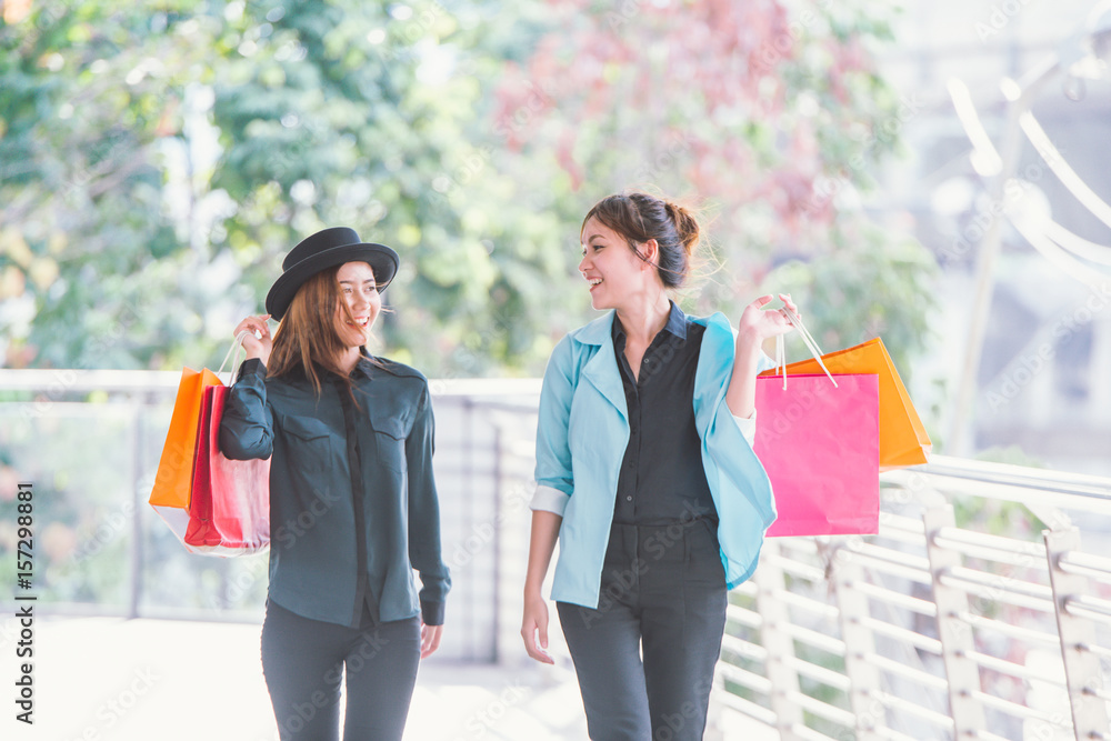 sale, consumerism and people concept - happy young women looking into shopping bags at shop in city.