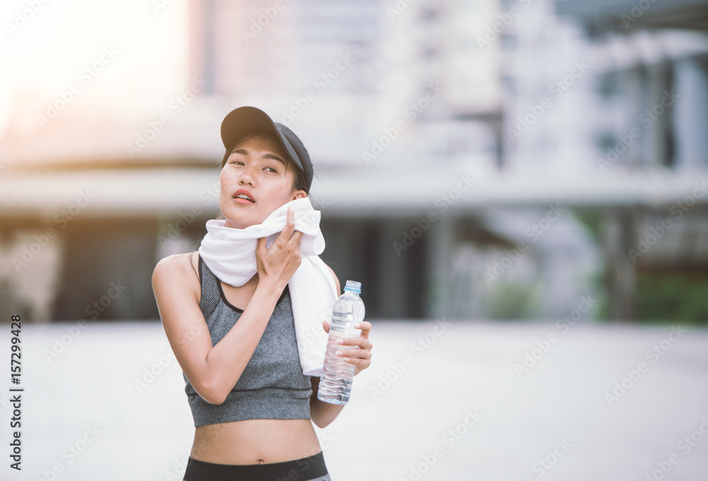 擦汗口渴的女性慢跑者训练后喝淡水。年轻的运动女性锻炼