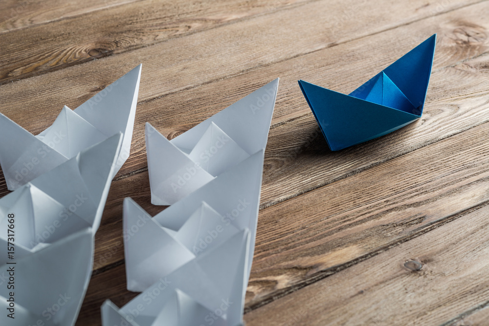 Business leadership concept with white and color paper boats on wooden table