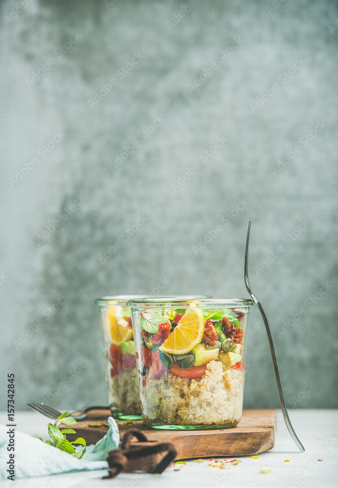 Healthy salad with quionoa, avocado, dried tomatoes, basil, mint, orange in glass jars on wooden boa