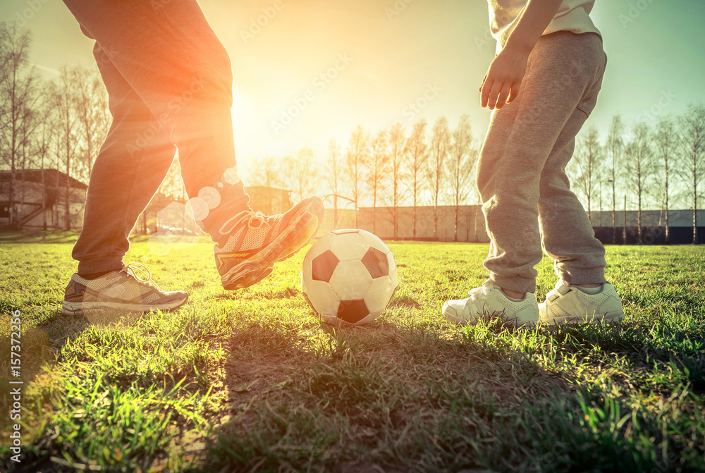 Father and son playing together with ball in football under sun