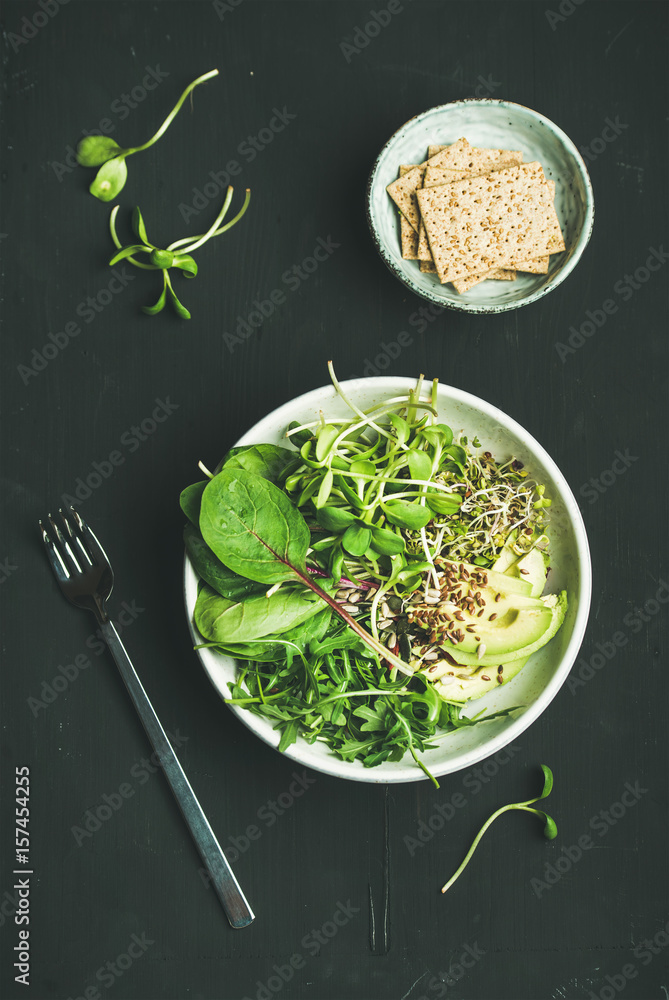 Green vegan breakfast meal in bowl with spinach, arugula, avocado, seeds and sprouts and crispy brea