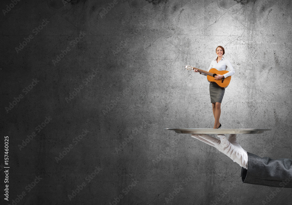 Attractive businesswoman on metal tray playing acoustic guitar against concrete wall background